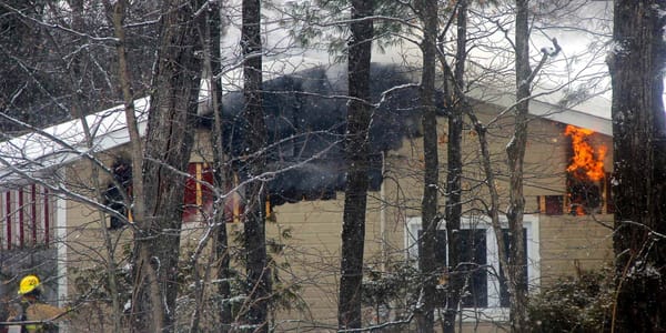 À travers bois, on devine des flammes dans la structure de la maison du chemin Pierre-Péladeau, à Sainte-Adèle, le 28 janvier